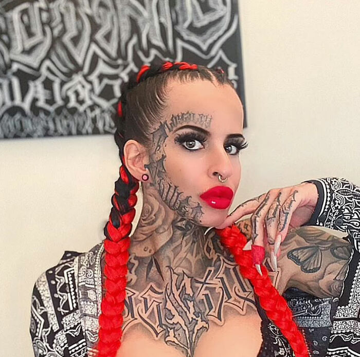 Tattooed woman with red braided hair and bold makeup, posing confidently, related to viral nose removal transformation.