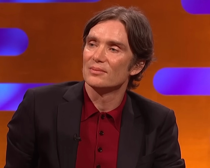 Cillian Murphy on the Graham Norton Show, wearing a black blazer and red shirt during a TV interview segment.