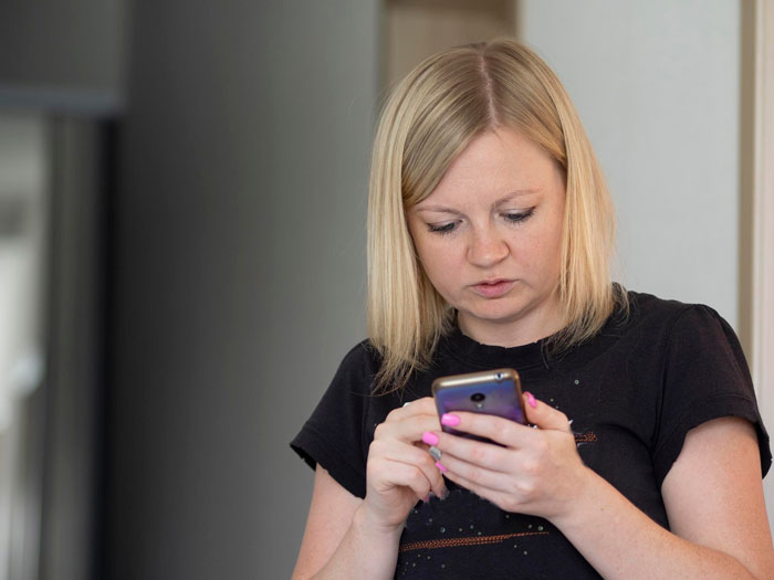 Woman with blonde hair wearing black shirt, looking at smartphone, texting and sharing screenshots about former student situation.