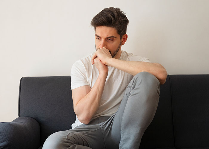 Thoughtful man sitting on a couch, reflecting deeply on empathy after a difficult conversation with his partner.