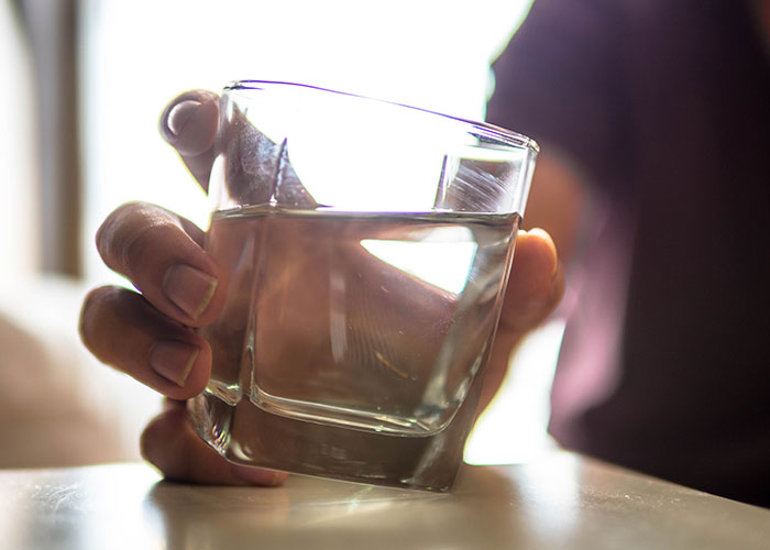 Close-up of a woman&rsquo;s hand holding a glass of water, symbolizing empathy and a tense moment with her boyfriend.