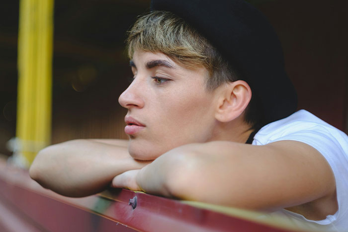 Teen boy wearing a dark cap resting his arms and looking away, reflecting feelings related to caring for a disabled son. Teen boy wearing a dark cap resting his arms and looking away, reflecting feelings related to caring for a disabled son.