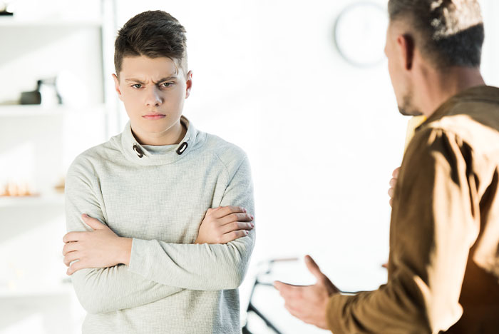 Teenage boy with arms crossed looking angry while talking to a man, reflecting frustration in caring for disabled son. Teenage boy with arms crossed looking angry while talking to a man, reflecting frustration in caring for disabled son.