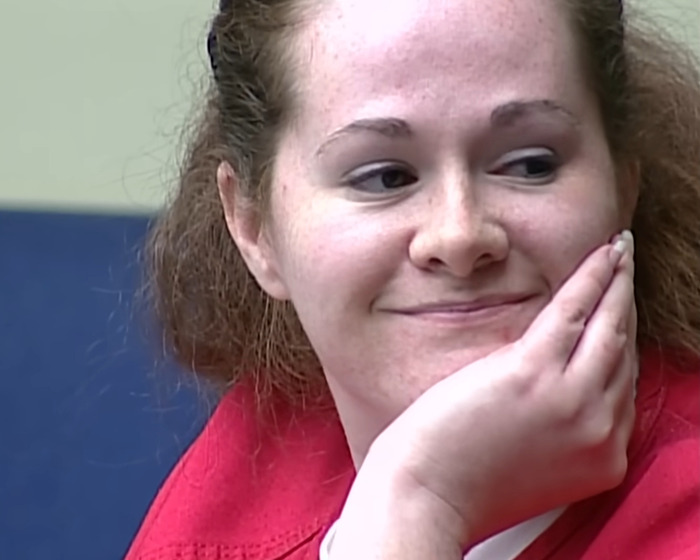 Woman in a red shirt sitting and smiling slightly, related to capital punishment for stabbing and pentagram carving case.