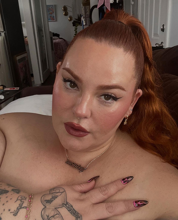 Plus-size model with red hair and flame nail art exposing fat-shaming by flight attendant mid-flight in a candid indoor selfie.