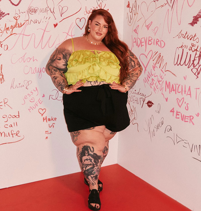 Plus-size model posing confidently against a graffiti-covered wall, showcasing tattoos and bold fashion style.