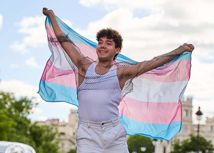 Person joyfully holding a transgender pride flag outdoors, symbolizing identity and freedom during Thanksgiving season.
