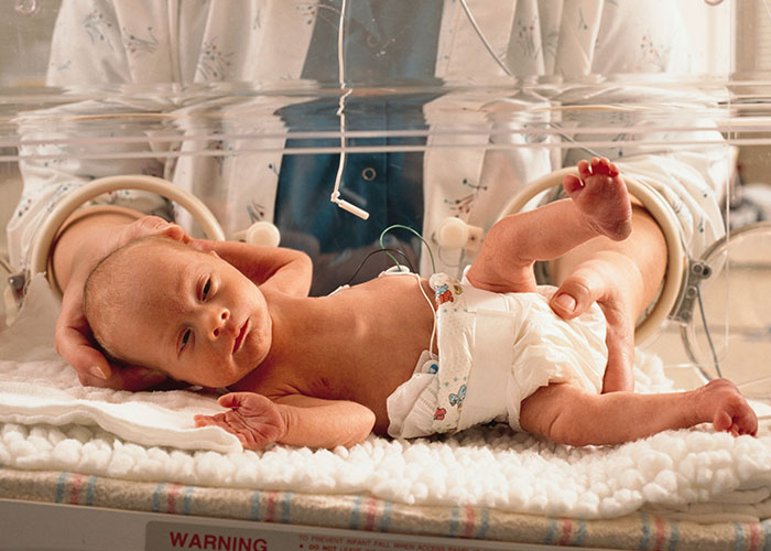 Premature newborn lying in an incubator receiving medical care representative of family and Thanksgiving stress themes.