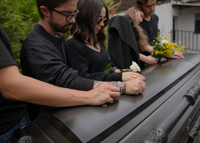 Group of people dressed in black, mourning and holding flowers at a coffin, reflecting miserable Thanksgiving and divorce feelings.