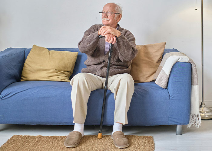 Elderly man sitting alone on a blue couch looking thoughtful, reflecting feelings of divorce and misery on Thanksgiving.