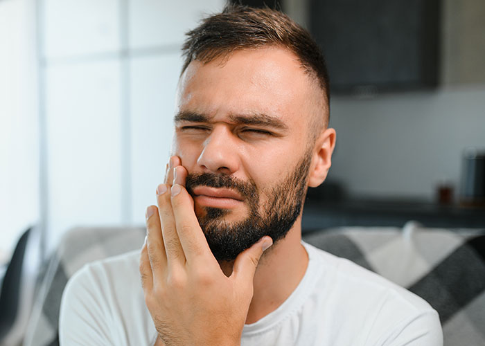 Man with a beard grimacing in pain, holding his cheek, illustrating misery during Thanksgiving divorce struggles.