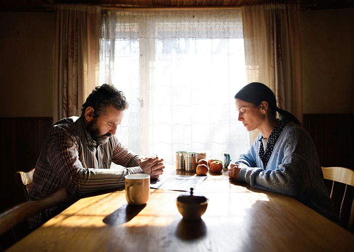 A couple sitting at a kitchen table in silence, showing tension and unhappiness on Thanksgiving day.