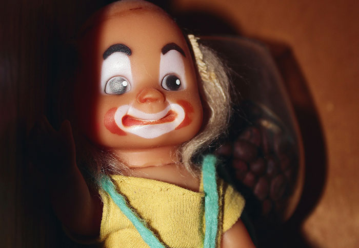 Close-up of a vintage clown doll with painted face and yellow outfit, perfect for moments people realized they aren’t supposed to see.