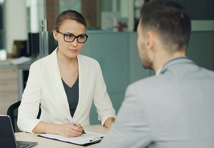 Woman in glasses and white blazer interviewing a man in a gray jacket, capturing a moment people realized they weren’t supposed to see.