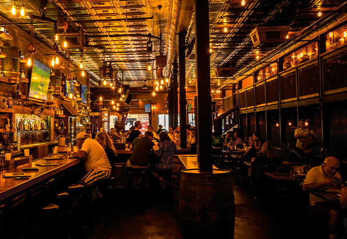 Dimly lit bar interior with people sitting, featuring vintage decor and warm hanging lights in a crowded setting.