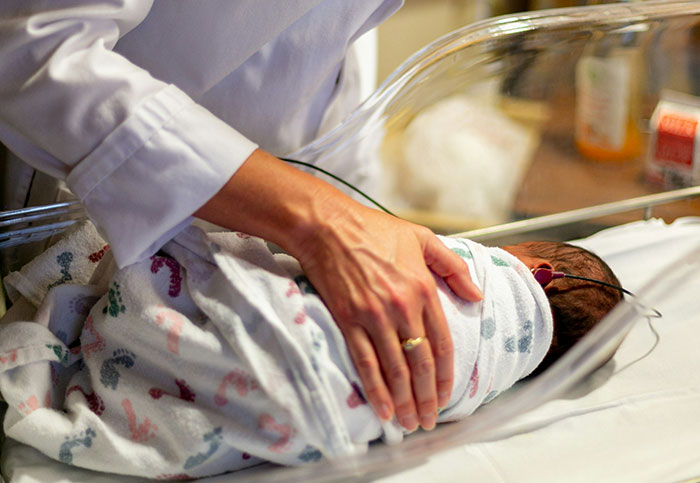 Medical professional gently placing a swaddled newborn in a hospital bassinet, an unexpected moment to see.