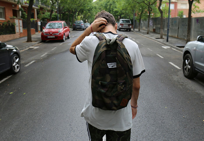 Teenager with camouflage backpack standing confused on empty street, capturing moments people realized they aren’t supposed to see.