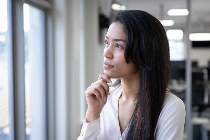 Young woman in white blouse looking thoughtfully out a window, representing simple car stuff skills and learning.