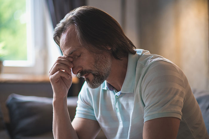 Middle-aged man in a striped polo shirt looking stressed and contemplative, representing husband unattracted to plastic surgery wife.