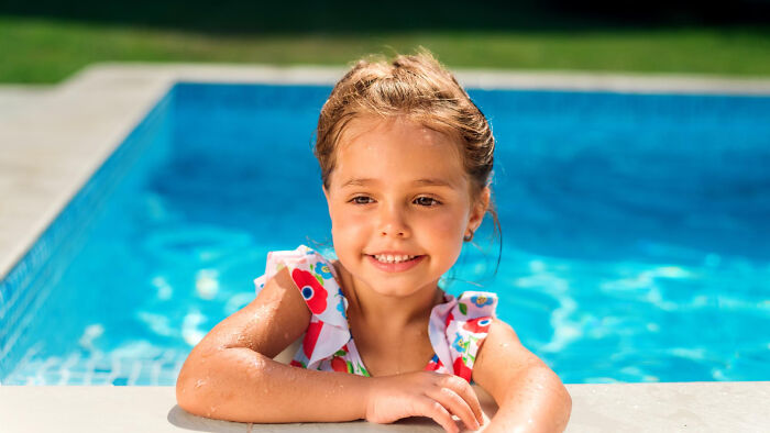 Young girl smiling while resting on the edge of a pool, capturing a moment for tired mom and let down dad.