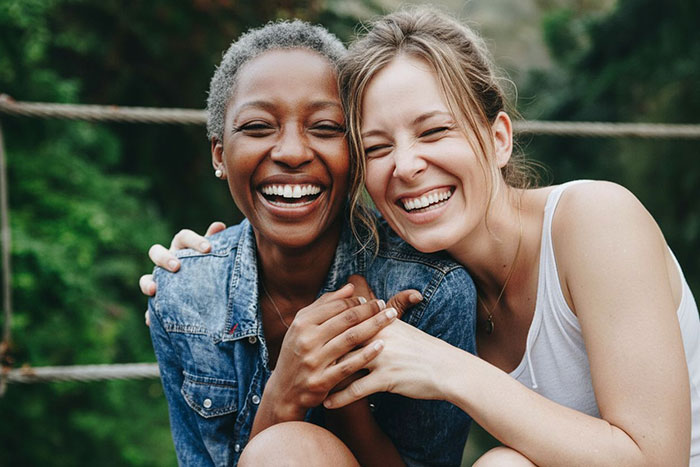 Two women laughing closely together outdoors, illustrating a woman facing challenges with her miracle baby adoption.