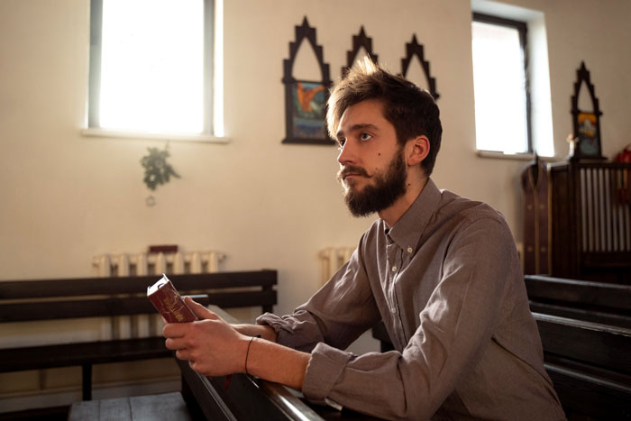 Religious man holding a book in a church, reflecting on faith, causing tension with coworkers at work.