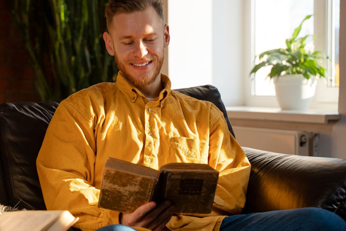 Man in yellow shirt reading a book indoors, illustrating a religious man pushing beliefs on coworkers at work.