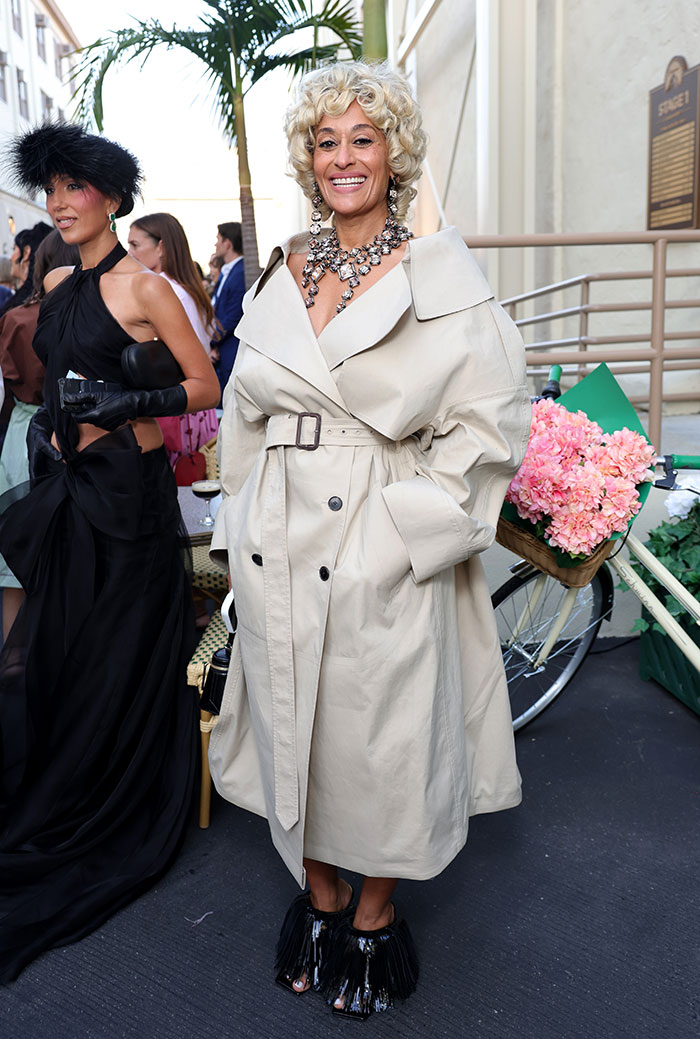 Woman wearing oversized beige trench coat and statement jewelry at Vogue World Hollywood, featuring weirdest celebrity looks.