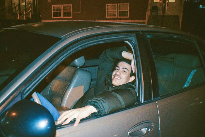 Teen boy smiling confidently while sitting in a car at night, illustrating shocking things popular kids did in school.