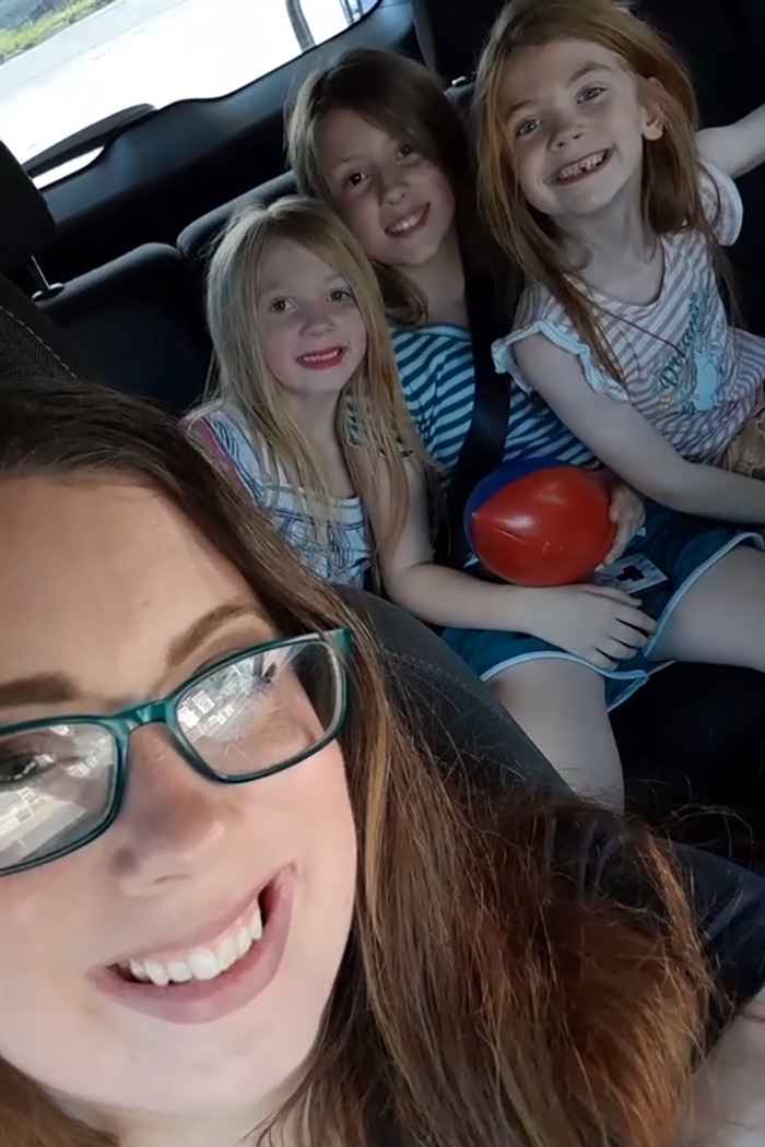 Woman with glasses smiling in car with three happy little sisters, highlighting heartmelting hospital gesture for surgery support.
