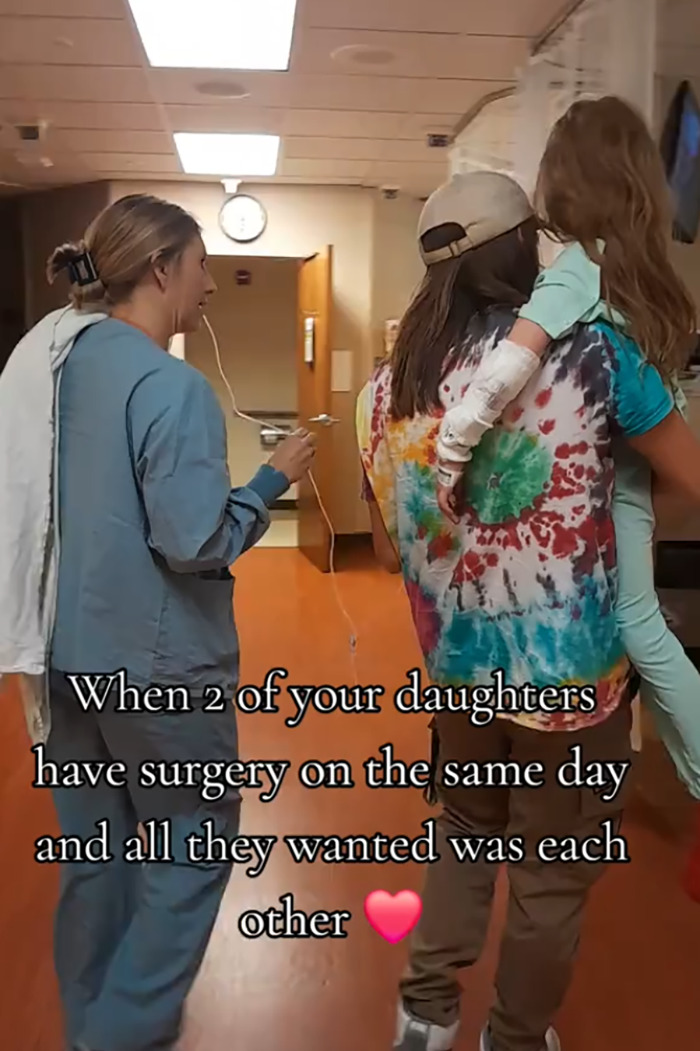 Hospital staff walking with a woman carrying a child, showing heartmelting gesture for two little sisters needing surgery.