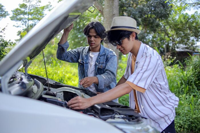 Two young men working on a car engine outdoors demonstrating simple car stuff skills for easy maintenance.