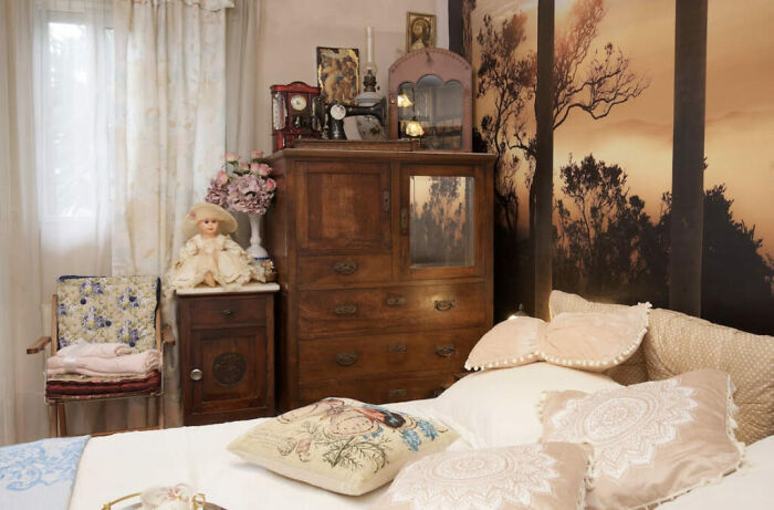 Vintage bedroom with 50 dolls, wooden furniture, and floral decor in a chaotic fairytale Airbnb setting.