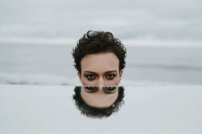 Person with curly hair partially hidden behind a reflective surface, creating a mirrored effect in an abstract setting for unpopular opinions poll.