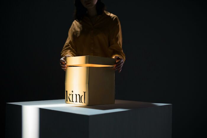 Person lifting lid of glowing box labeled kind in a dark room, representing unpopular opinions poll concept.