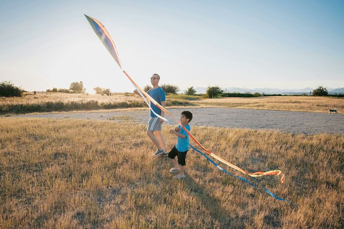 Father and son flying a colorful kite together outdoors in a field during golden hour for unpopular opinions poll 4.
