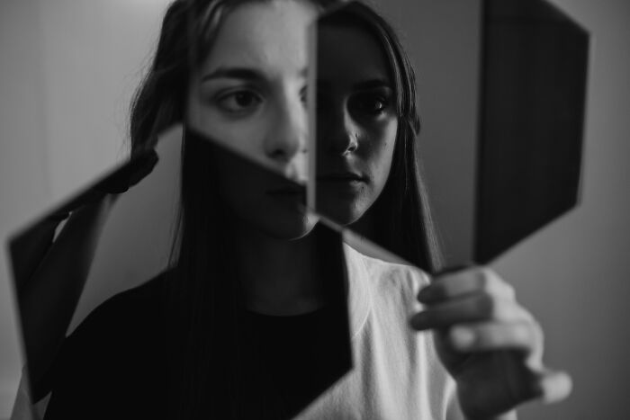 Young woman holding broken mirror shards reflecting fragmented face in a moody black and white unpopular opinions poll setting.