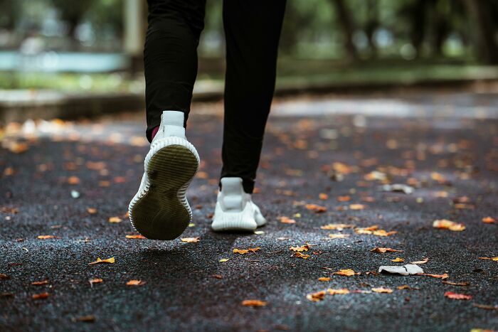 Person walking on a leaf-covered path wearing white sneakers and black pants outdoors for unpopular opinions poll 4.