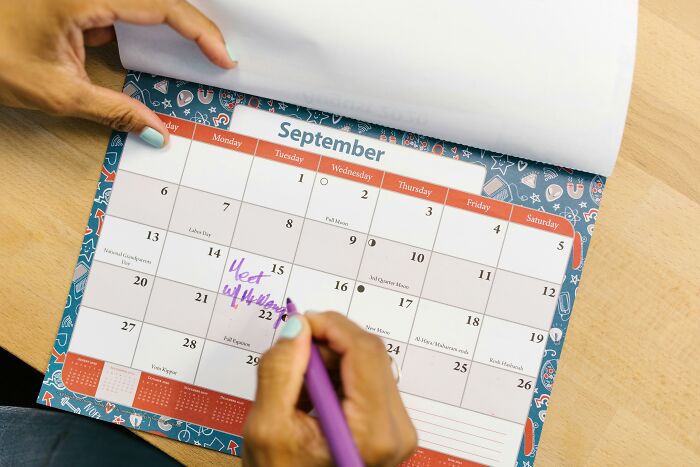 Person writing on a September calendar with purple pen, planning events for unpopular opinions poll 4 discussion.