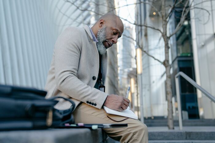 Man sitting outdoors writing in a notebook, capturing thoughts for unpopular opinions poll in an urban setting.