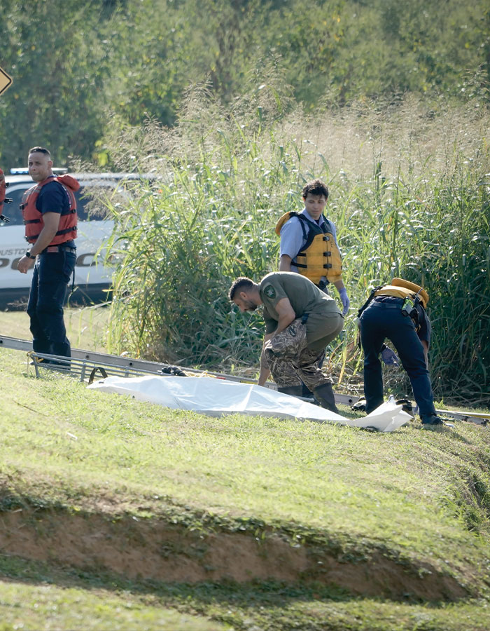 Law enforcement officers at a crime scene near tall grass as fears of serial criminal rise in Houston after 16th body found.