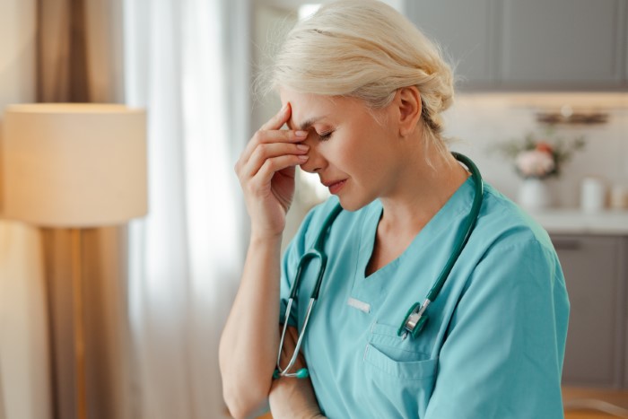 Doctor in scrubs with stethoscope looking stressed while touching forehead, depicting refusal to rehire sister after costly mistake.