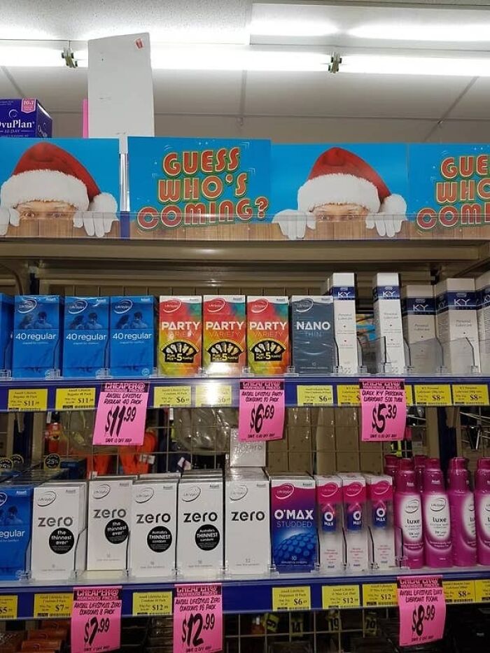 Shelf of condoms with a humorous Guess Who's Coming sign featuring Santa hats, highlighting accidental comedy in retail displays.