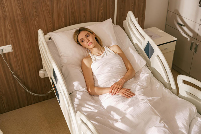 Young woman lying in hospital bed looking upset before planned surgery during surprise family visit organized by boyfriend