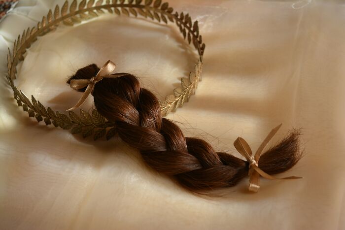 Braided brown hair tied with ribbons placed inside a gold laurel wreath on a light fabric, symbolizing disastrous playdates.