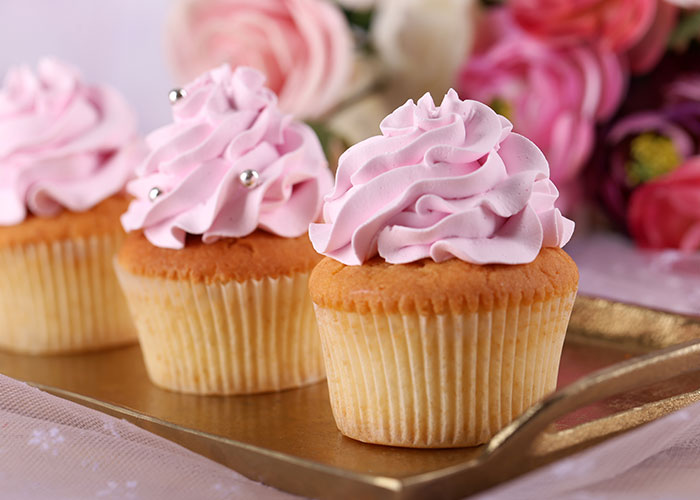 Three pink frosted cupcakes on a tray with flowers in the background representing wedding vendors and allergy concerns.