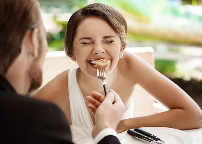Bride smiling with eyes closed being fed a small piece of dessert by groom, highlighting wedding vendors and allergy issues.