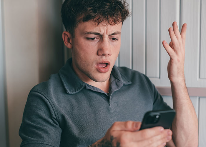 Young man reacting with frustration while looking at his phone, illustrating wedding vendors leaving bride with no cupcakes due to allergy