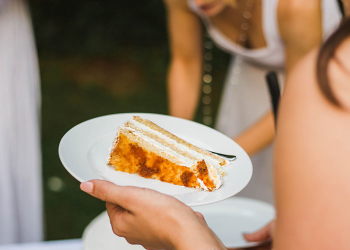 Bride holding a plate with a slice of wedding cake, highlighting wedding vendors and allergy cupcake issues.