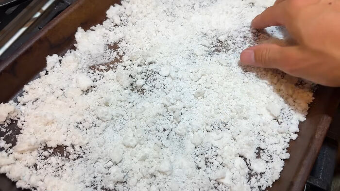 Hand spreading a layer of coarse salt on a baking tray as part of a life hack trick that requires extra work.